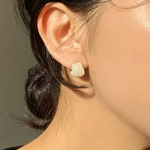 Close-up of minimalist creamy white irregular stud earring worn by a model in soft light