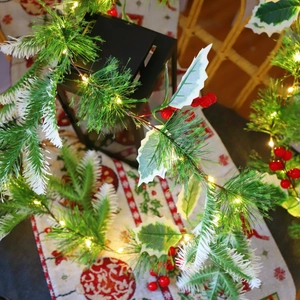 Close-up of pine needle garland with red berries and warm LED lights in a cozy room