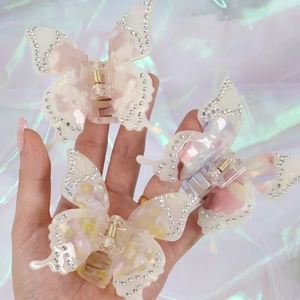 Three acetate butterfly hair claws with rhinestones held by a hand on laser background