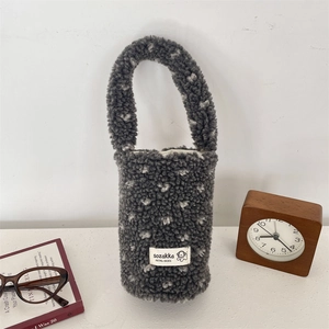 Detail of plush grey heart-pattern drink carrier next to glasses and a vintage clock
