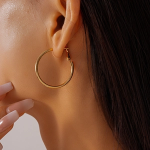Close-up of polished gold-finish oversized hoop earrings worn on a model's side profile