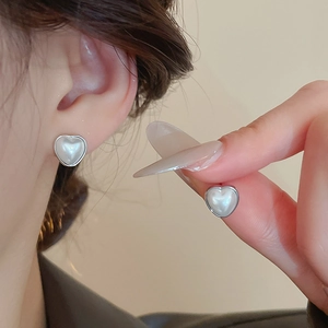 Détail des boucles d'oreilles cœur en perles argentées portées à l'oreille et à la main