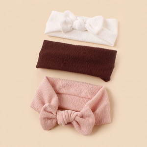 Close-up of three textured knit baby headbands in white, brown, and pink colors