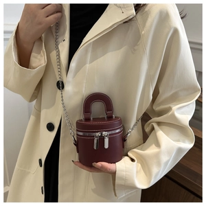 Gros plan d'un mini sac cylindre bordeaux avec chaîne argentée sur un trench beige