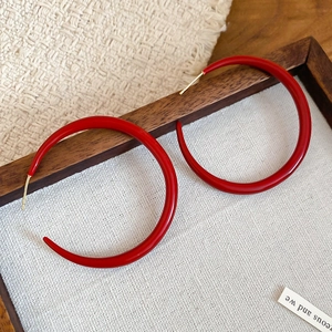 Detail view of large red enamel hoop earrings on rustic wood and woven fabric background