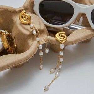 Elegant gold spiral stud earrings with long white pearl tassels on a minimalist tray