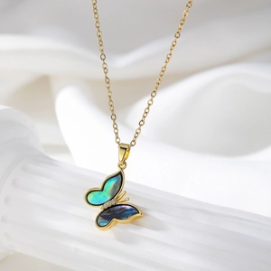 Detailed shot of golden butterfly pendant with iridescent shell wings on white silk