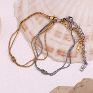 Detail of gold and silver knot snake chain bracelets on white shell with water drops