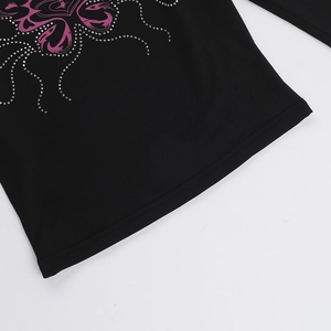 Dettaglio della maglia nera a maniche lunghe con stampa farfalla viola e strass argento