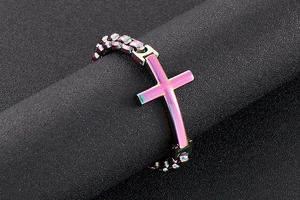 Detailed view of iridescent cross charm on a steel link bracelet with rainbow finish