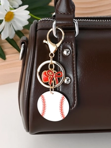 Detail of baseball charm and golden heart love pendant hanging on a leather bag