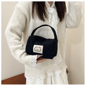Detail of a black corduroy handbag with a cute cartoon bear patch held by a model