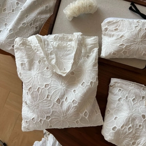 White cotton tote bag with hollow floral embroidery and matching zipper pouch on wood