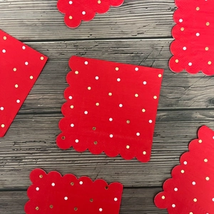 Red scalloped paper napkins with gold and white polka dots on dark wood background