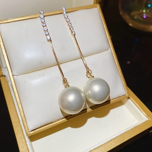 Close-up of elegant gold tassel earrings with shimmering crystals and a large white pearl