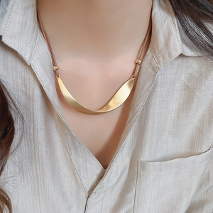 Close-up of a gold irregular twisted metal pendant with brown leather cord on a model