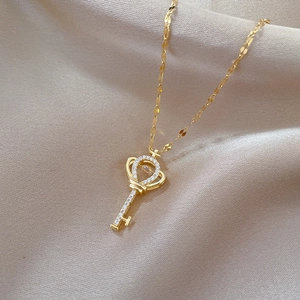 Macro shot of gold key pendant with sparkling heart zircon on champagne silk fabric