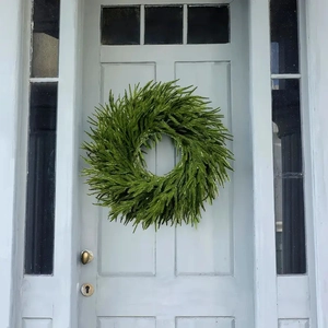 Deep green artificial cedar wreath hanging on a light blue wooden door as festive decor