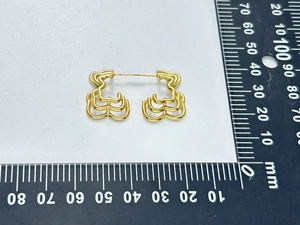 Macro detail of bear-shaped hollow earrings with measurement ruler in gold finish