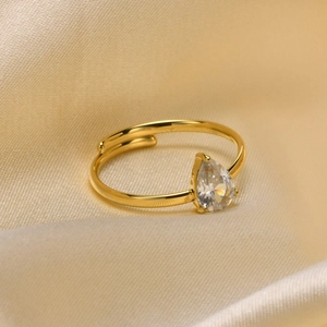 Close-up of golden teardrop zircon ring with three-prong setting on champagne silk cloth