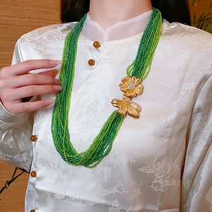 Detail of multilayer green seed bead necklace with gold floral and butterfly clasp accents