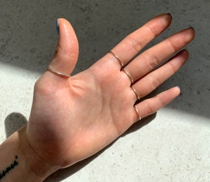Close-up of five thin minimalist silver stackable bands worn on fingers in sunlight