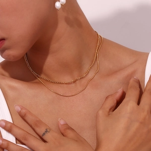 Close-up of double layered gold figaro and snake chains with pearl earrings on a model