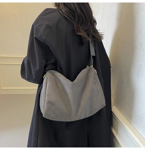 Detail of grey suede baguette bag with gold zippers worn over a black winter coat