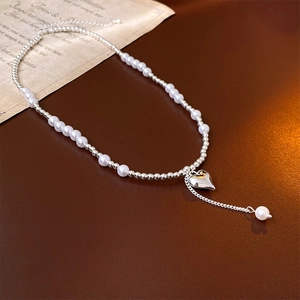 Detail of silver heart pendant with pearl and bead chain on dark leather background
