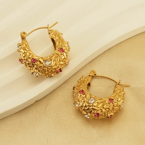 Detail of 18K gold-plated hoop earrings with woven texture and pink crystals on a tray