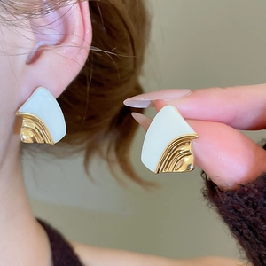 Detailed close-up of geometric fan-shaped earrings with gold ridges and cream enamel