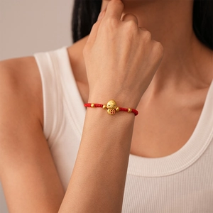 Detailed close-up of a red woven zodiac snake bracelet with golden charms on a female wrist