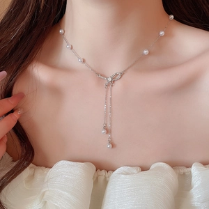 Close-up of bowknot pearl pendant necklace with diamond tassels worn on elegant neckline