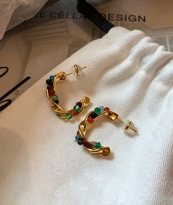 Detail of gold C-shaped hoop earrings with colorful beads on a white cotton pouch