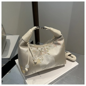 Close-up of floral embroidery on beige satin handbag with gold metal clasp handle