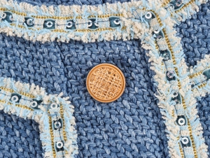 Detail eines blauen Tweedkleids mit goldenem Knopf und goldfarbenem Paillettenbesatz