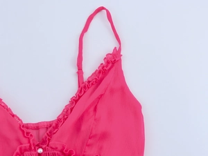 Gros plan sur une robe en mousseline rose avec bords volantés et détail de perle
