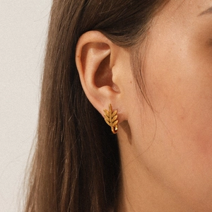 Close-up of gold leaf-shaped stud earrings worn on the ear to show details and size