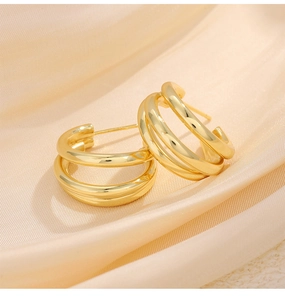 Macro shot of three-layer intertwined golden hoop earrings on beige silk fabric background