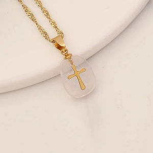 Macro shot of gold twist chain with a transparent resin cross pendant on white surface