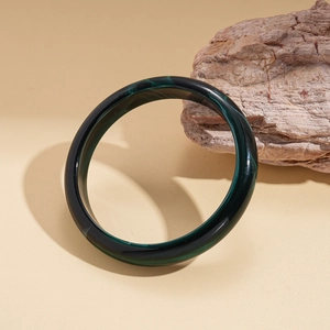 Détail d'un bracelet en acrylique vert émeraude avec texture marbrée noire sur fond beige