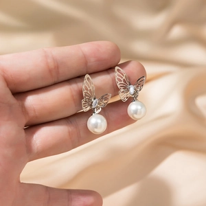 Elegant hollow butterfly drop earrings with white pearls on a champagne silk background