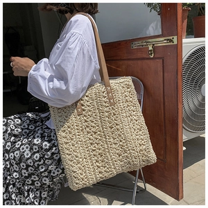 Detail of woven straw tote bag with brown leather straps and X-shape stitching craftsmanship