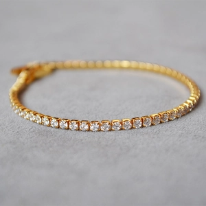 Detailed close-up of a gold-plated tennis bracelet featuring a single row of sparkling zircons