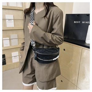 Detail of black pleated crescent bag with pearl chain and wavy strap worn as crossbody