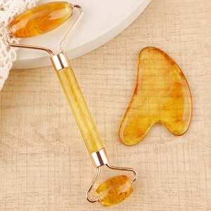 Detailed amber resin facial roller and heart-shaped gua sha tool on a wooden surface