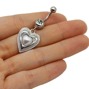 Detail shot of heart belly ring with white pearl and zircon held by hand for size