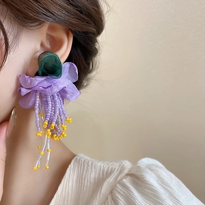 Gros plan de boucles d'oreilles fleurs à pompons violets et feuilles vertes sur mannequin