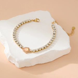 Gold tennis bracelet with heart pendant and square zircons on stone background