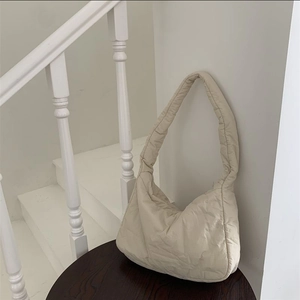 Minimalist beige quilted nylon tote bag displayed on a vintage dark wooden stool